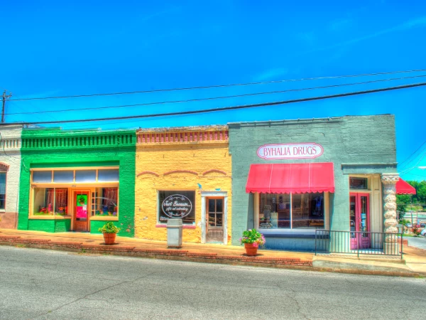 Brightly painted storefronts on Main Street in Byhalia, MS, including “Byhalia Drugs” under a red awning, surrounded by potted flowers and clear blue skies — reflecting small-town character and commercial energy needs.