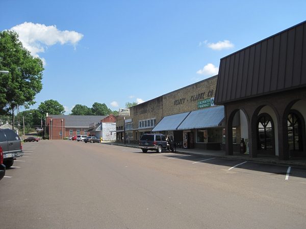 Quiet downtown street in Coldwater, MS, lined with brick storefronts including “Valley Clarke Co.” and “Coldwater Pharmacy,” under a clear blue sky — showcasing small-town commerce powered by modern electrical systems.