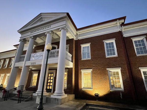 The elegant brick facade of the BankTennessee building in Collierville, TN, illuminated at dusk with white columns and a classic pediment — representing the town’s historic charm and modern needs.