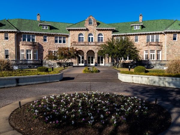 The grand stone facade of the historic Chisca Hotel in Cordova, TN, featuring green-tiled roofs, arched windows, and a circular driveway with blooming flower beds.