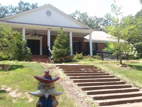 A charming brick home with white columns and a welcoming front porch in DeSoto County, surrounded by greenery and featuring a whimsical garden gnome.