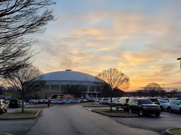 The FedExForum arena glowing under a golden sunset sky, surrounded by parked cars and leafless trees — a landmark of East Memphis, TN.