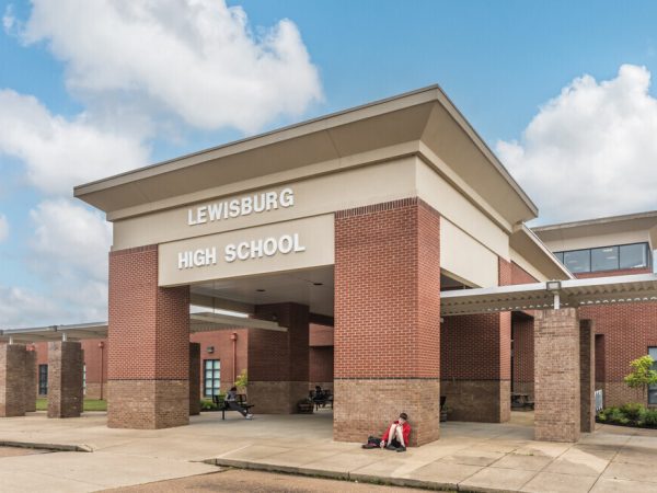 Modern brick entrance to Lewisburg High School with students relaxing under a covered walkway — symbolizing the importance of reliable, safe electrical systems in educational facilities.
