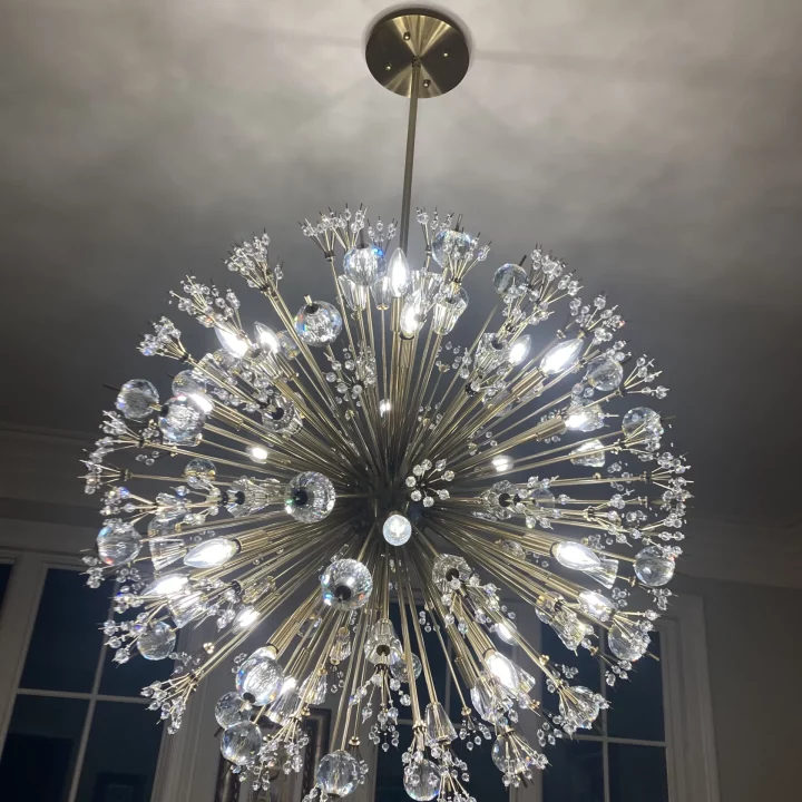 Luxurious chandelier with multiple crystal embellishments and radiant lights, hanging from the ceiling of a well-decorated room.