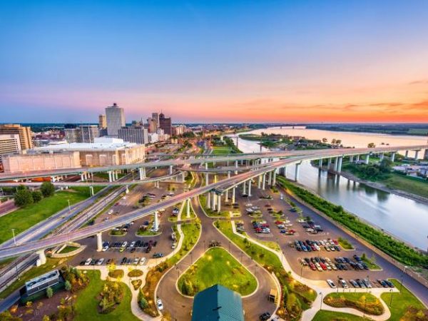 Aerial view of downtown Memphis at dusk, showcasing highway interchanges, riverfront parks, and the iconic Hernando de Soto Bridge spanning the Mississippi River.
