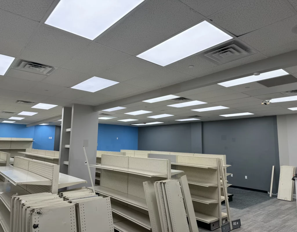 An empty commercial space prepared for fit-out, with shelving units in place and a newly installed ceiling with LED lights.