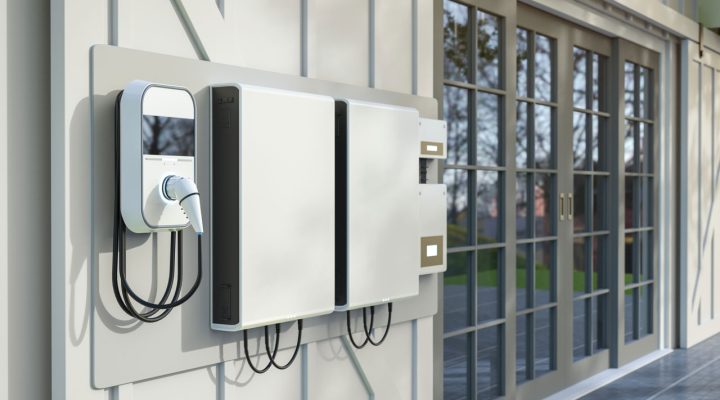 White wall-mounted battery storage units with an electric vehicle charger installed on a modern home exterior.
