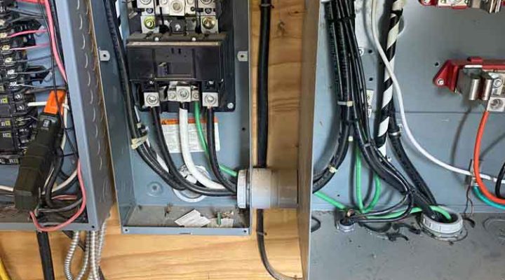 Close-up of an open electrical panel with multiple colored wires and breakers being serviced.