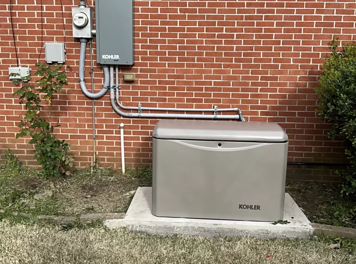 A Kohler generator installed on a concrete pad with electrical connections on the exterior of a brick building.