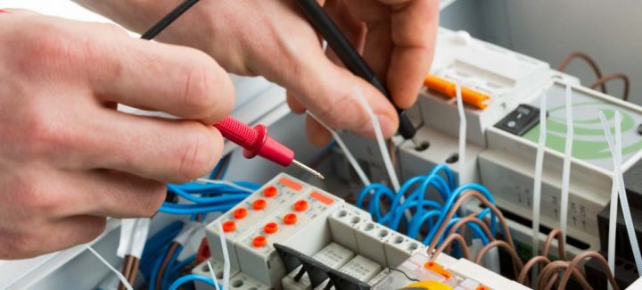Hands of an electrician with multimeter probe at an electrical switchgear cabinet
