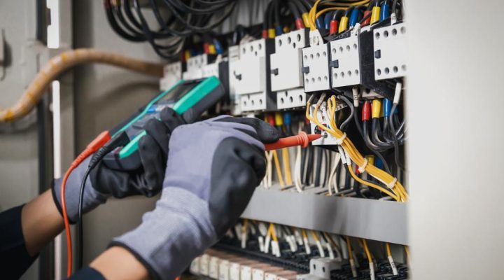 Electrician using a multimeter to diagnose and repair an electrical panel with multiple wires and breakers