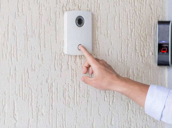 Hand of a man in a white shirt pressing the button of a door bell on a white wall of a house, a smart door knocker with a video camera for communication